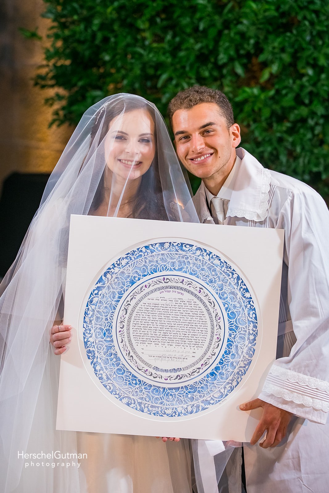 A couple smiling and holding their chosen Ketubah, symbolizing their love and commitment.